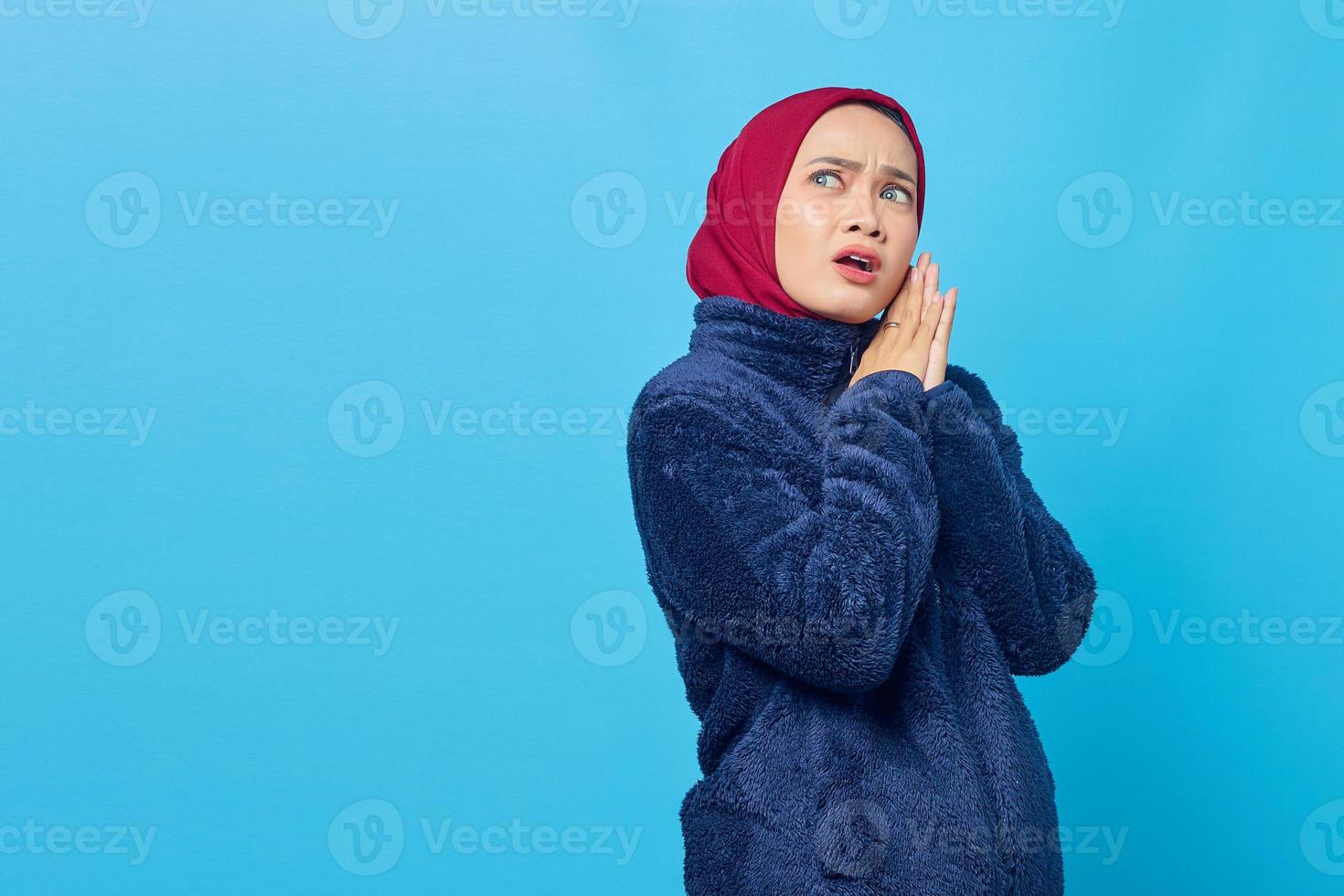 schockierte junge asiatische frau reibt sich die hände und schaut auf blauem hintergrund beiseite foto