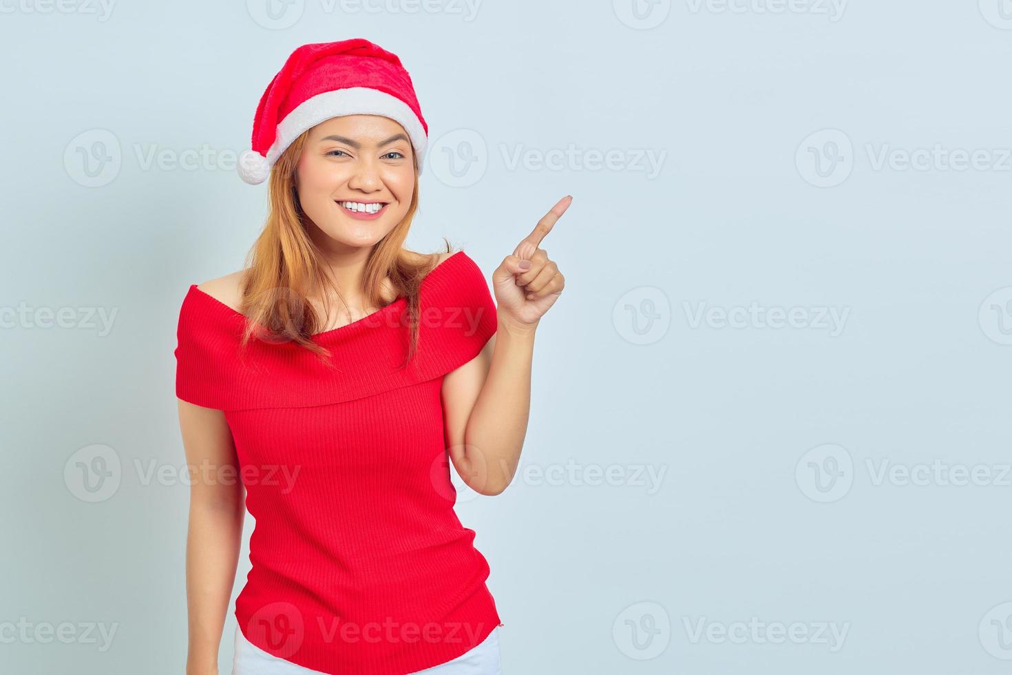 Porträt der jungen asiatischen Frau, die Weihnachtskleid trägt, lächelt und zeigt mit dem Finger auf den Kopierraum. Weihnachtskonzept foto