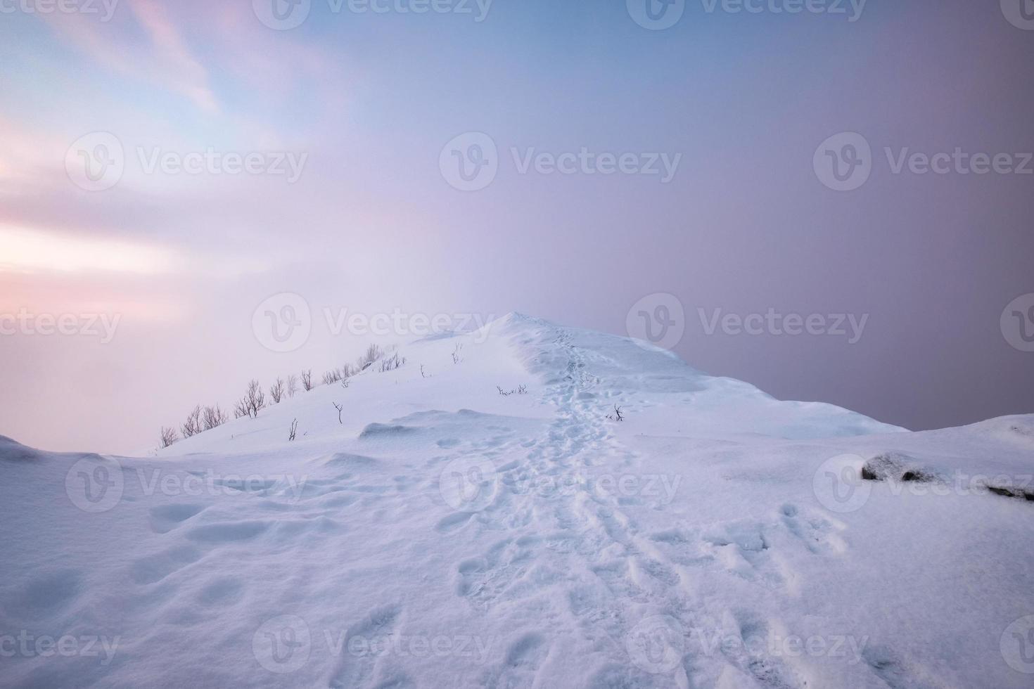 schneebedeckter Berggipfel mit Fußabdruck und buntem Himmel im Schneesturm auf dem Berg Segla auf der Insel Senja foto