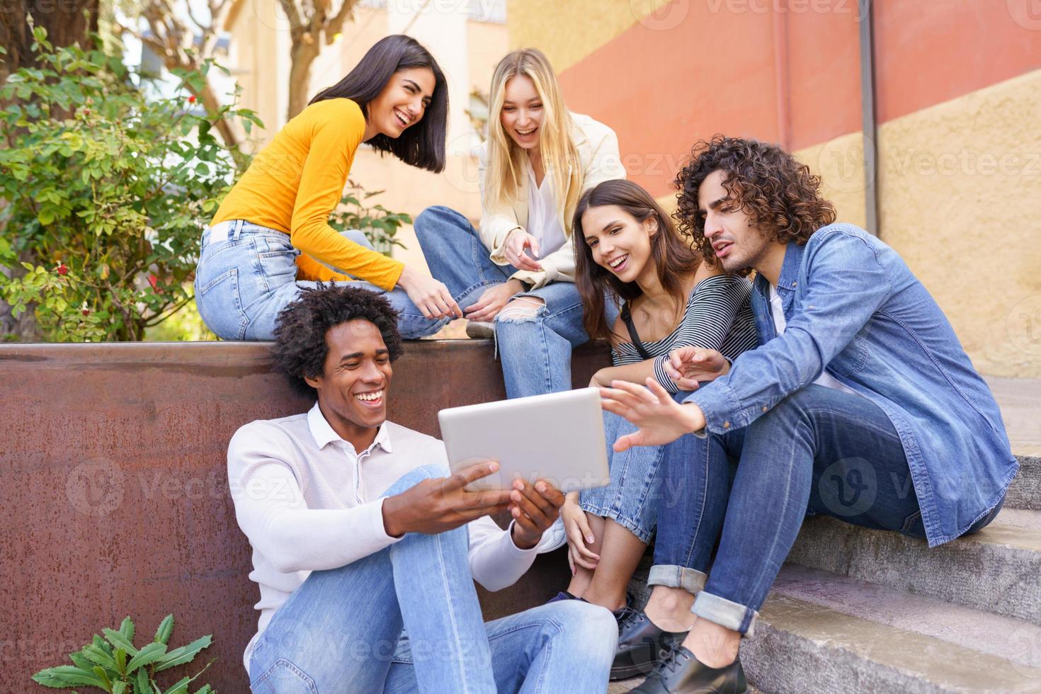 multiethnische Gruppe junger Menschen, die im Freien im städtischen Hintergrund ein digitales Tablet betrachten. foto