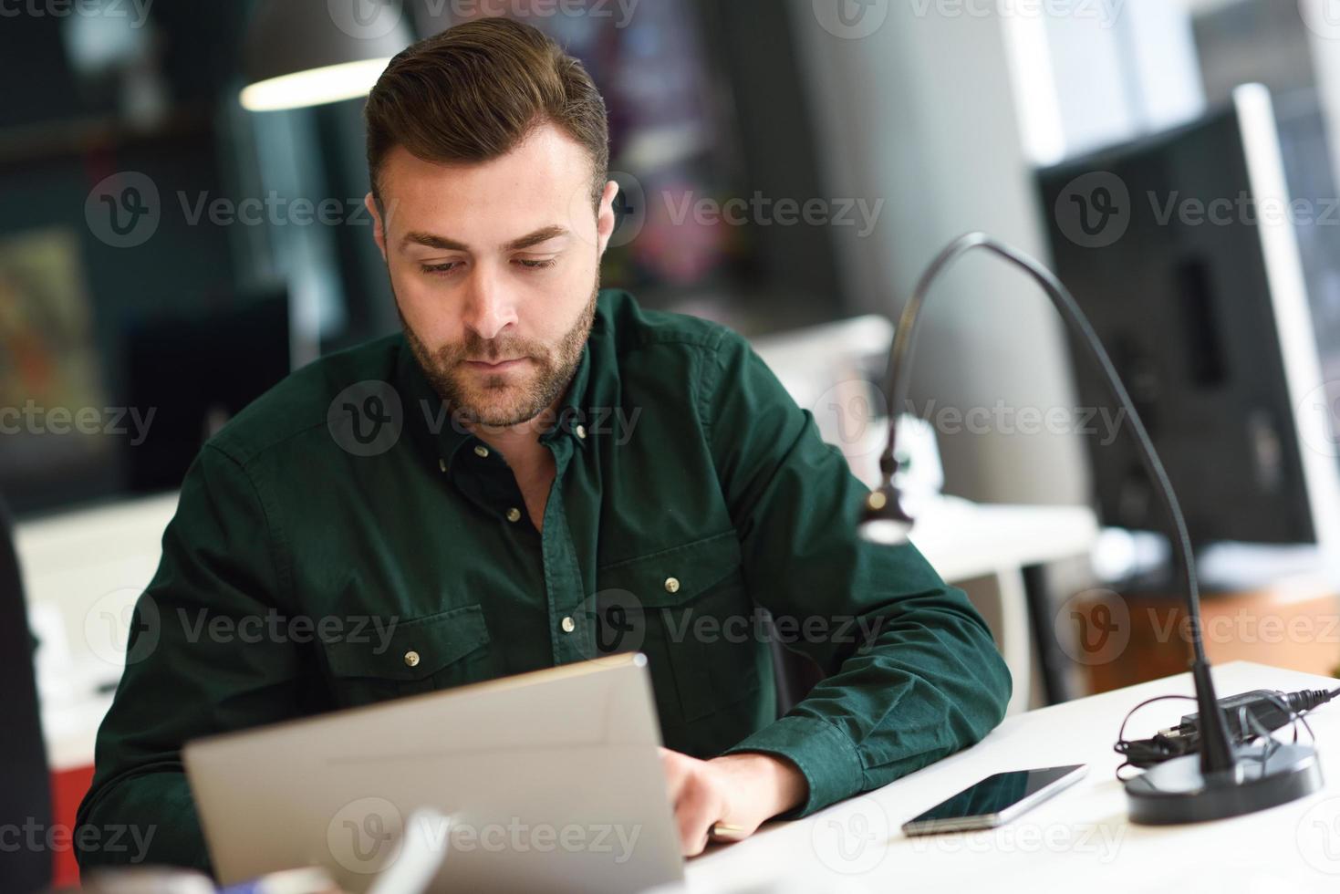 junger Mann, der mit Laptop-Computer auf weißem Schreibtisch studiert. foto