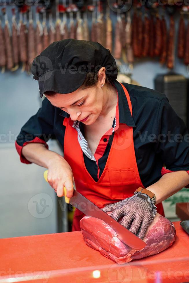 Frau schneidet frisches Fleisch in einer Metzgerei mit Metallsicherheitsnetzhandschuh foto