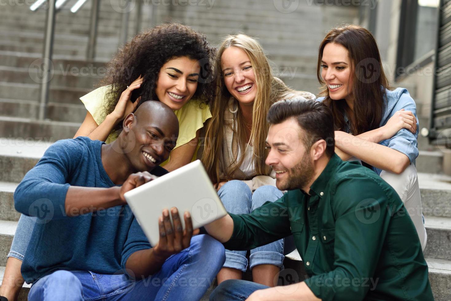 multiethnische Gruppe junger Menschen, die auf einen Tablet-Computer schauen foto