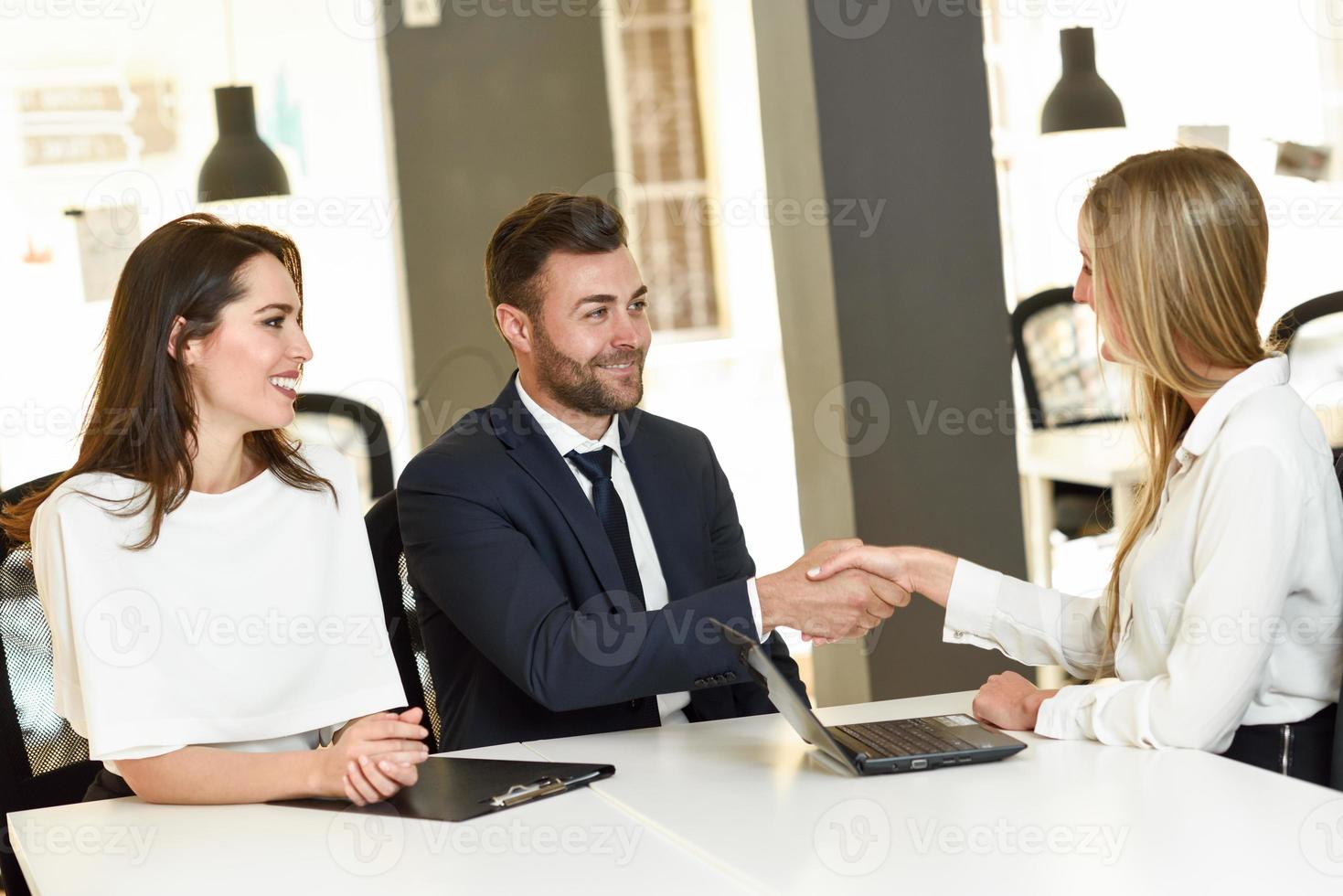 lächelndes junges Paar, das einem Versicherungsagenten die Hand schüttelt foto