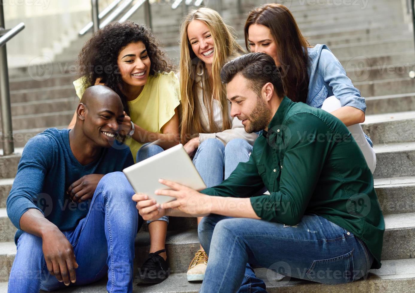 multiethnische Gruppe junger Menschen, die auf einen Tablet-Computer schauen foto