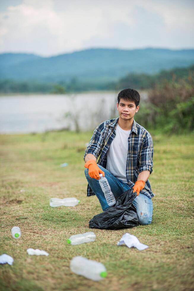 Ein Mann mit orangefarbenen Handschuhen sammelt Müll in einer schwarzen Tasche. foto