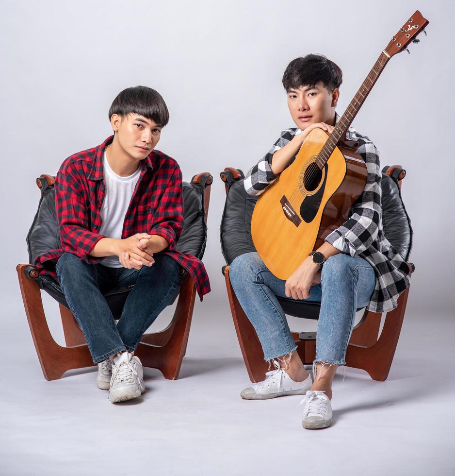 Zwei junge Männer sitzen auf einem Stuhl und halten eine Gitarre foto