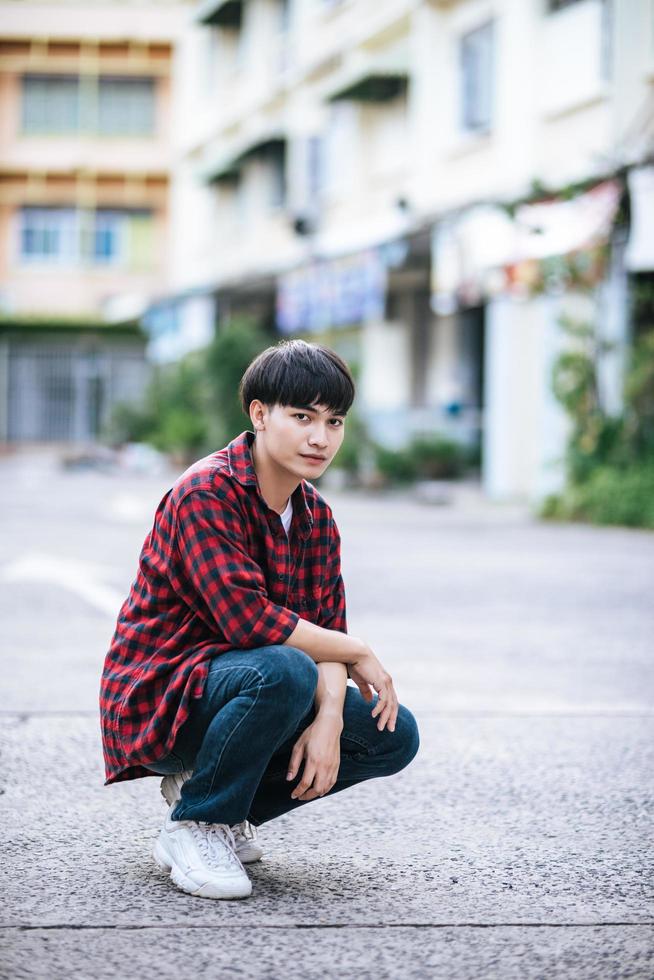 ein junger Mann in einem gestreiften Hemd sitzt auf der Straße foto