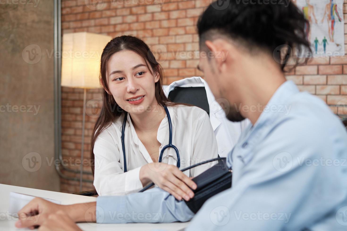 Schöne Ärztin in weißem Hemd, die eine asiatische Person mit Stethoskop ist, ist eine Gesundheitsprüfung eines männlichen Patienten in einer medizinischen Klinik mit Backsteinmauerhintergrund und lächelt, berät den Beruf des Facharztes. foto