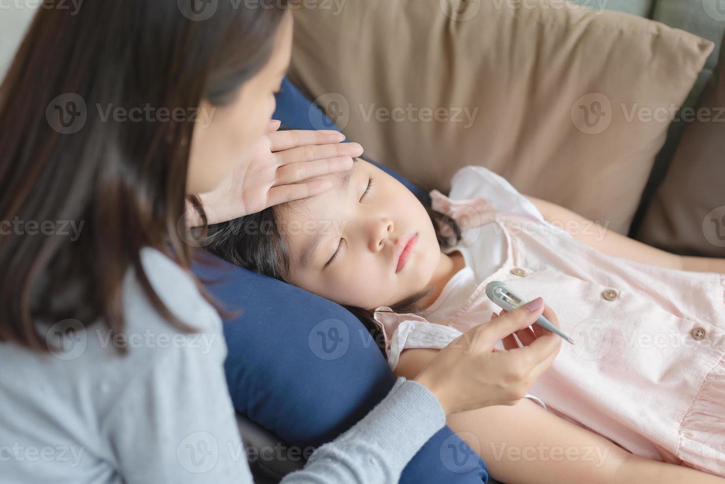 Asiatische Mutter, die die Körpertemperatur ihres Kindes mit einem Thermometer überprüft, das zu Hause Fieber und Krankheit bekam. foto