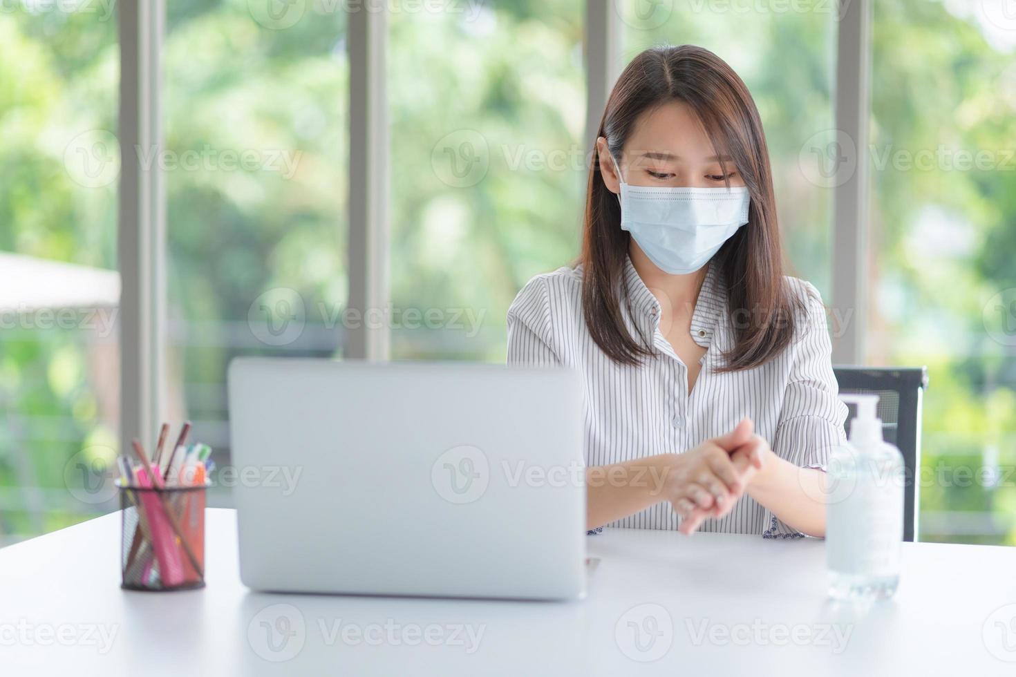 Geschäftsfrau, die Maske trägt und persönliches Desinfektionsmittel verwendet, um ihre Hand im Büro zu reinigen, um die Hygiene zu wahren. Präventiv während der Epidemie durch Coronavirus oder Covid19. foto