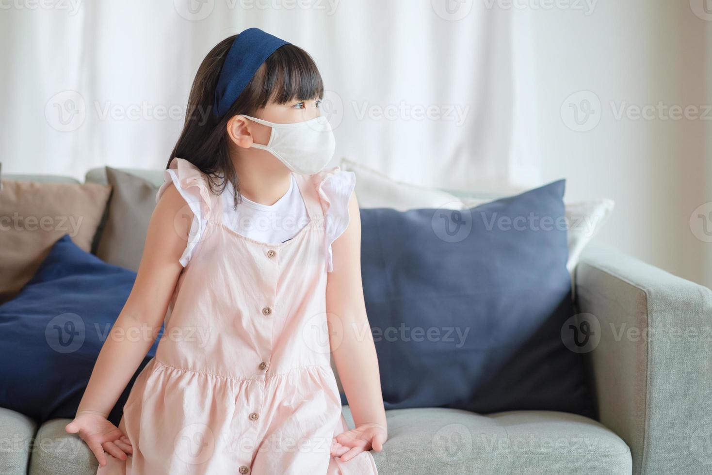 Asiatisches kleines süßes Mädchen, das eine hygienische Gesichtsmaske trägt, um den Ausbruch von Coronavirus oder Covid-19 zu verhindern, halten soziale Distanz und bleiben zu Hause. foto