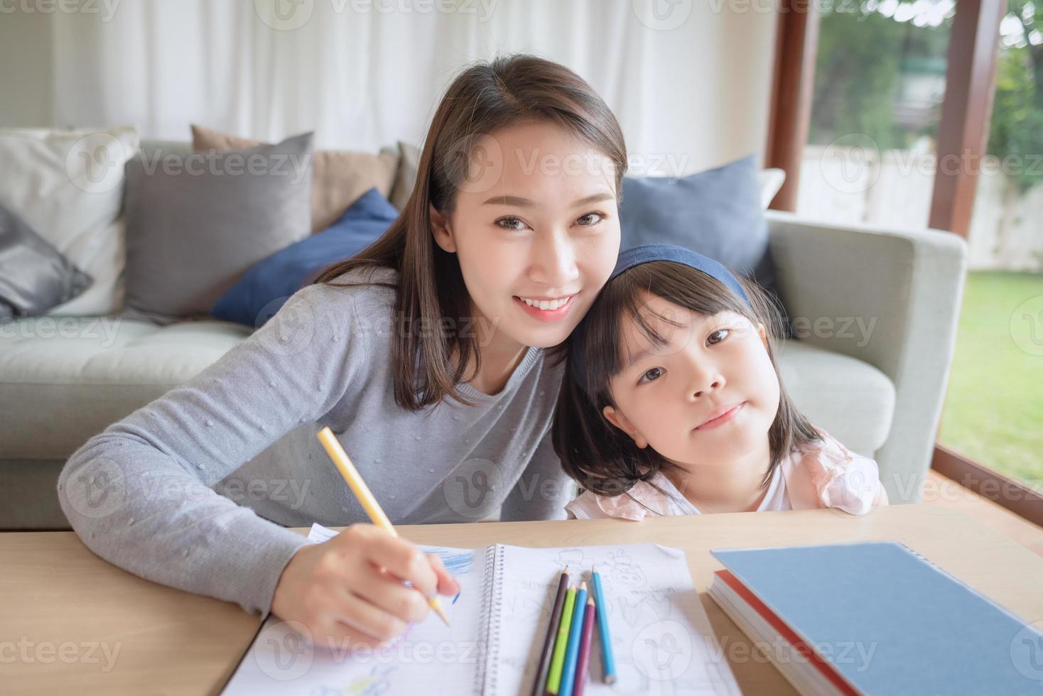 glückliche asiatische Mutter, die ihrer süßen Tochter das Studium der Vorschule im Wohnzimmer zu Hause beibringt foto