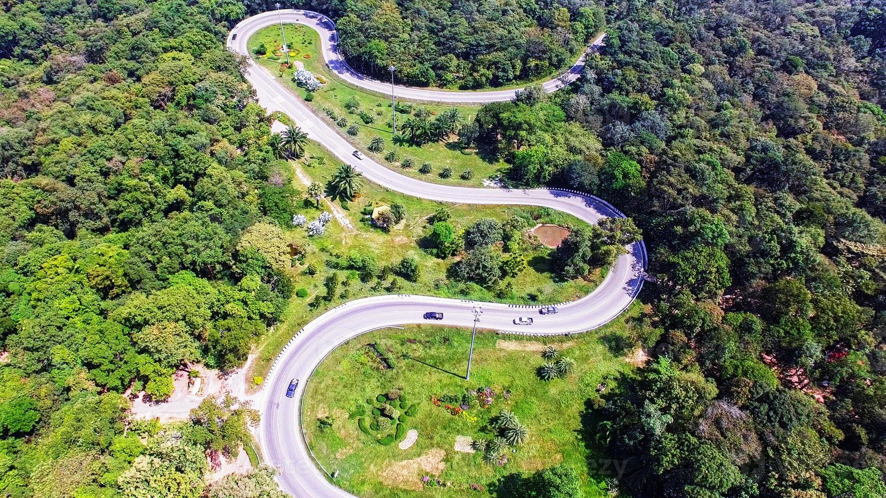 Luftaufnahme von der Drohne von Autos geht durch eine Kurvenstraße auf dem Berg mit grünem Wald. die Transportstraße über den Berg. foto