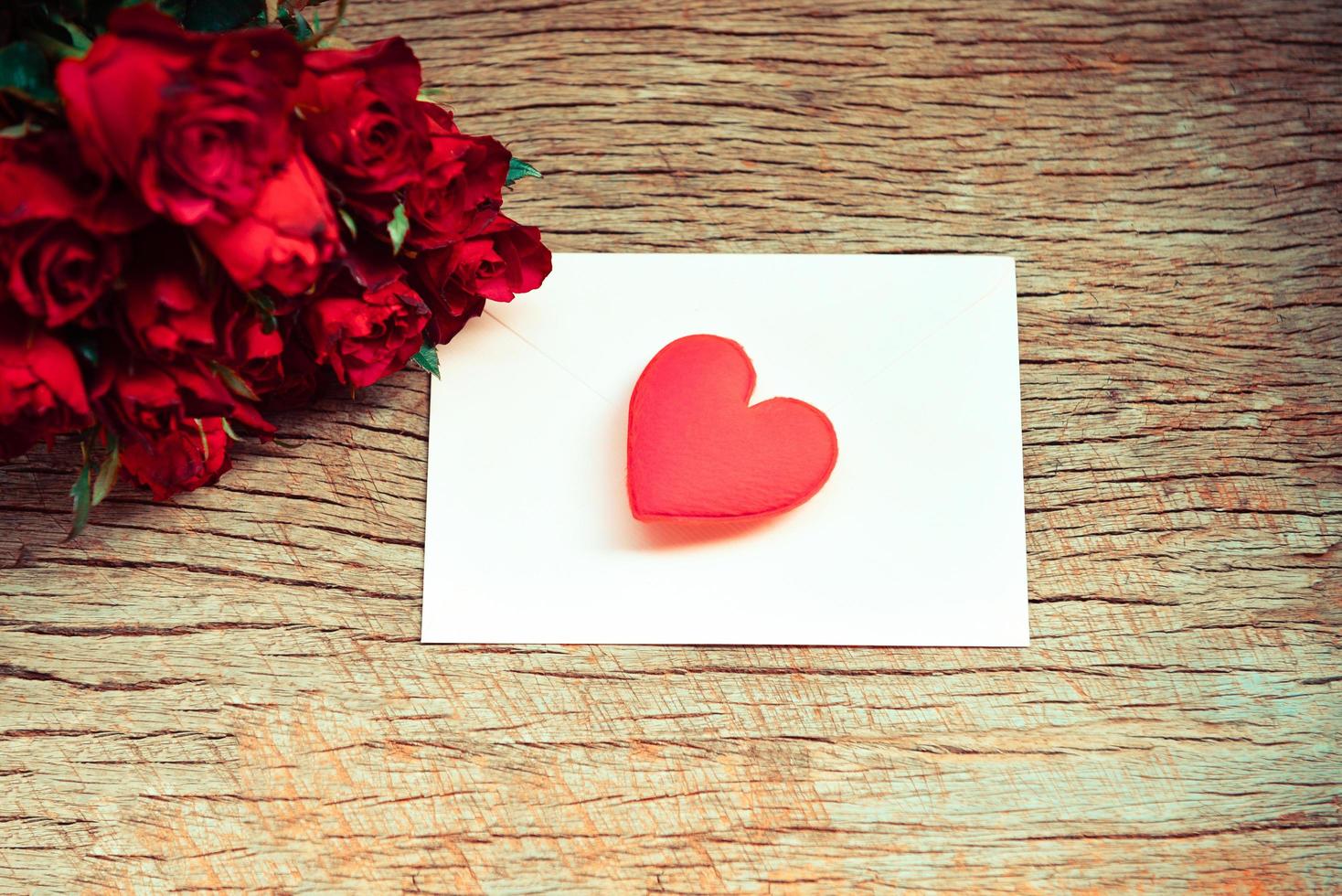 rote Rosen Blumenstrauß romantische Liebe Valentinstag Karte Umschlag Briefpost mit rotem Herzen - Einladungskarte Hochzeit auf Holz Hintergrund foto
