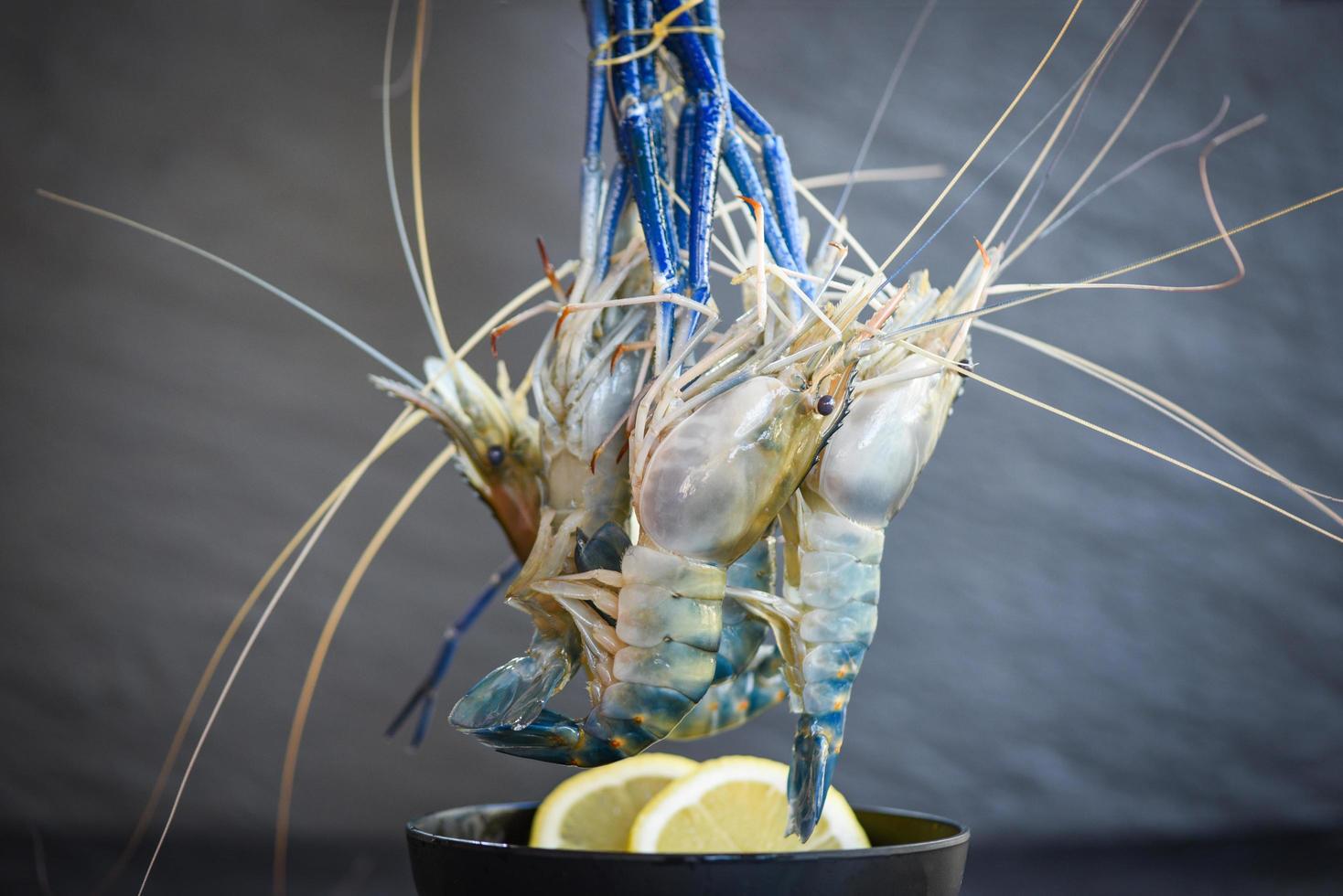 rohe Garnelen auf Schüssel mit Gewürzen Zitrone auf dunklem Plattenhintergrund - frische Garnelen für gekochtes Essen im Restaurant oder Fischmarkt foto