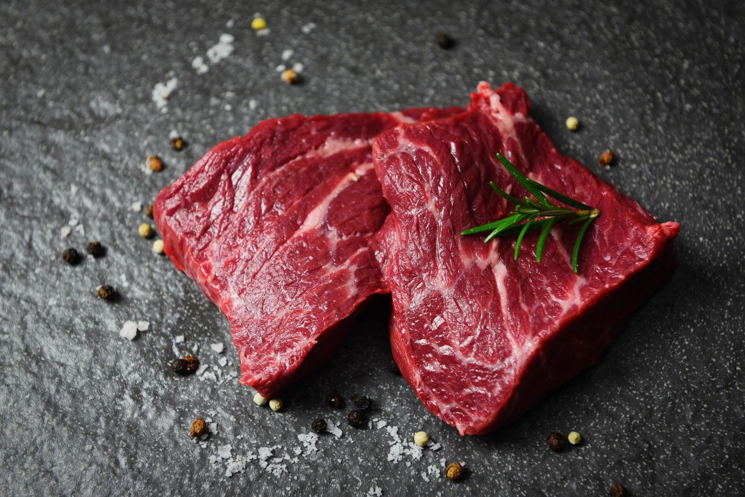 rohes Rindersteak mit Kräutern und Gewürzen - frisches Rindfleisch in Scheiben auf schwarzem Hintergrund foto