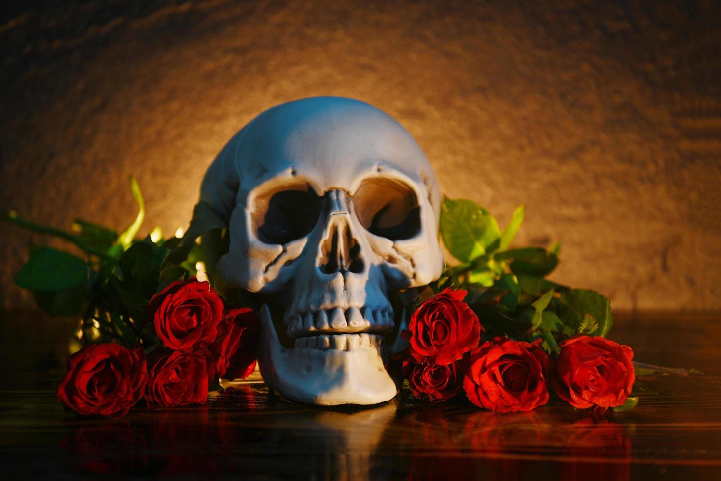 Rote Rosen Blumenstrauß auf rustikalem Holz mit Totenkopf und Kerzenlicht Hintergrund - Blumen Rose romantisches Liebes- und Todeskonzept zum Valentinstag foto