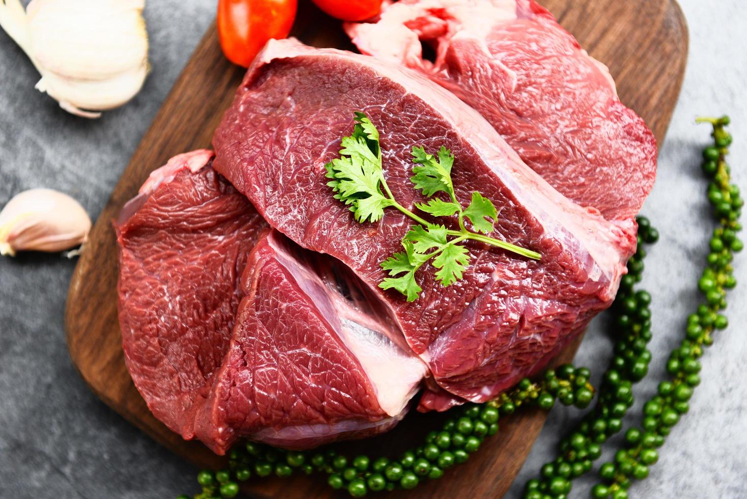rohes Rindfleisch auf Holzbrett auf dem Küchentisch zum Kochen von Rindersteak gebraten oder gegrillt mit Zutaten Kräuter und Gewürze frisches Rindfleisch tierisches Protein foto