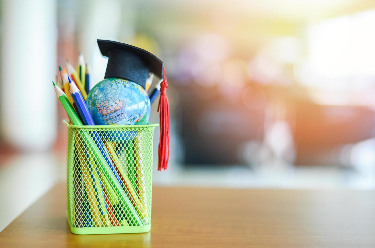 Abschlusshut auf der Erde Globusmodell Globales Bildungskonzept Bildung Lernen und zurück zur Schule mit Abschlusskappe auf einem Federmäppchen auf dem Tisch im Bibliothekshintergrund foto