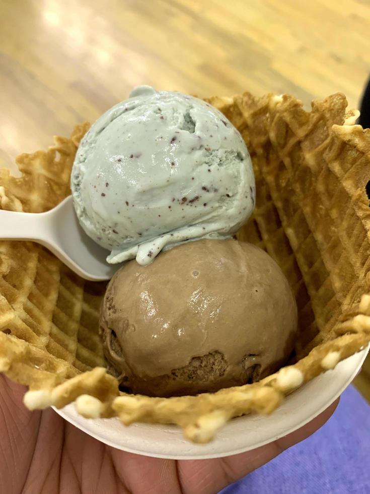 Eiscreme-Vanille- und Schokoladenaroma und Waffel-gefrorenes Dessertmuster in der weißen Tasse-Hand, die auf dem Tisch hält. foto