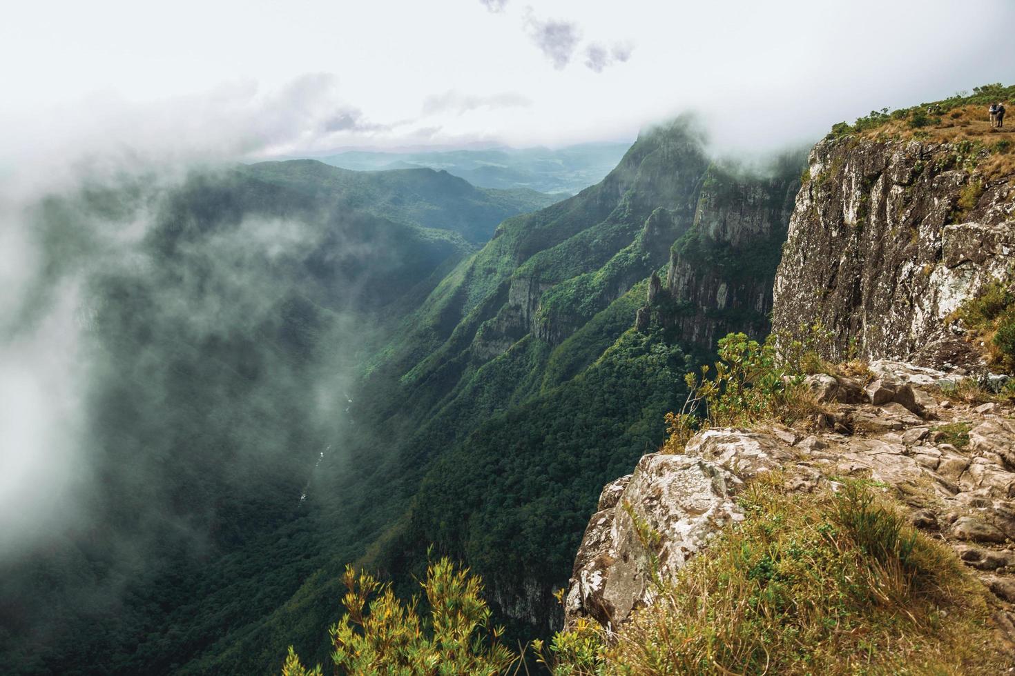 Menschen auf steilen Felsklippen in der Fortaleza-Schlucht, bedeckt von Wald und Nebel, der aus dem Tal in der Nähe von Cambara do Sul aufsteigt. eine kleine ländliche stadt im süden brasiliens mit erstaunlichen natürlichen touristenattraktionen. foto