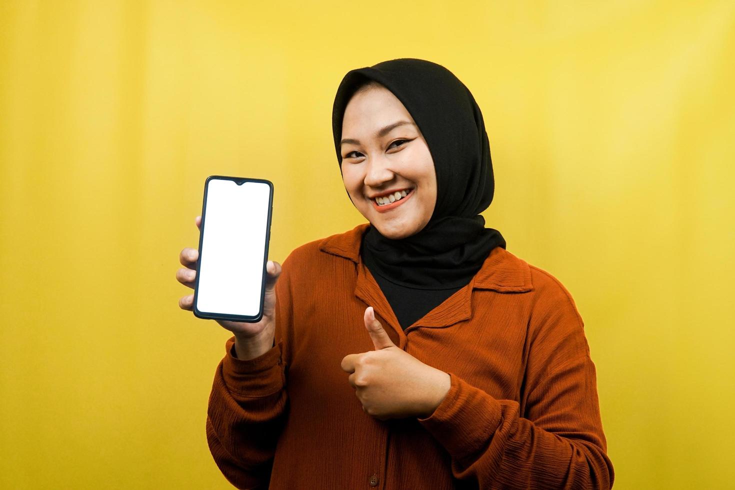 schöne junge asiatische muslimische frau, die ein smartphone mit weißem oder leerem bildschirm hält, app fördert, etwas fördert, isoliert, werbekonzept foto