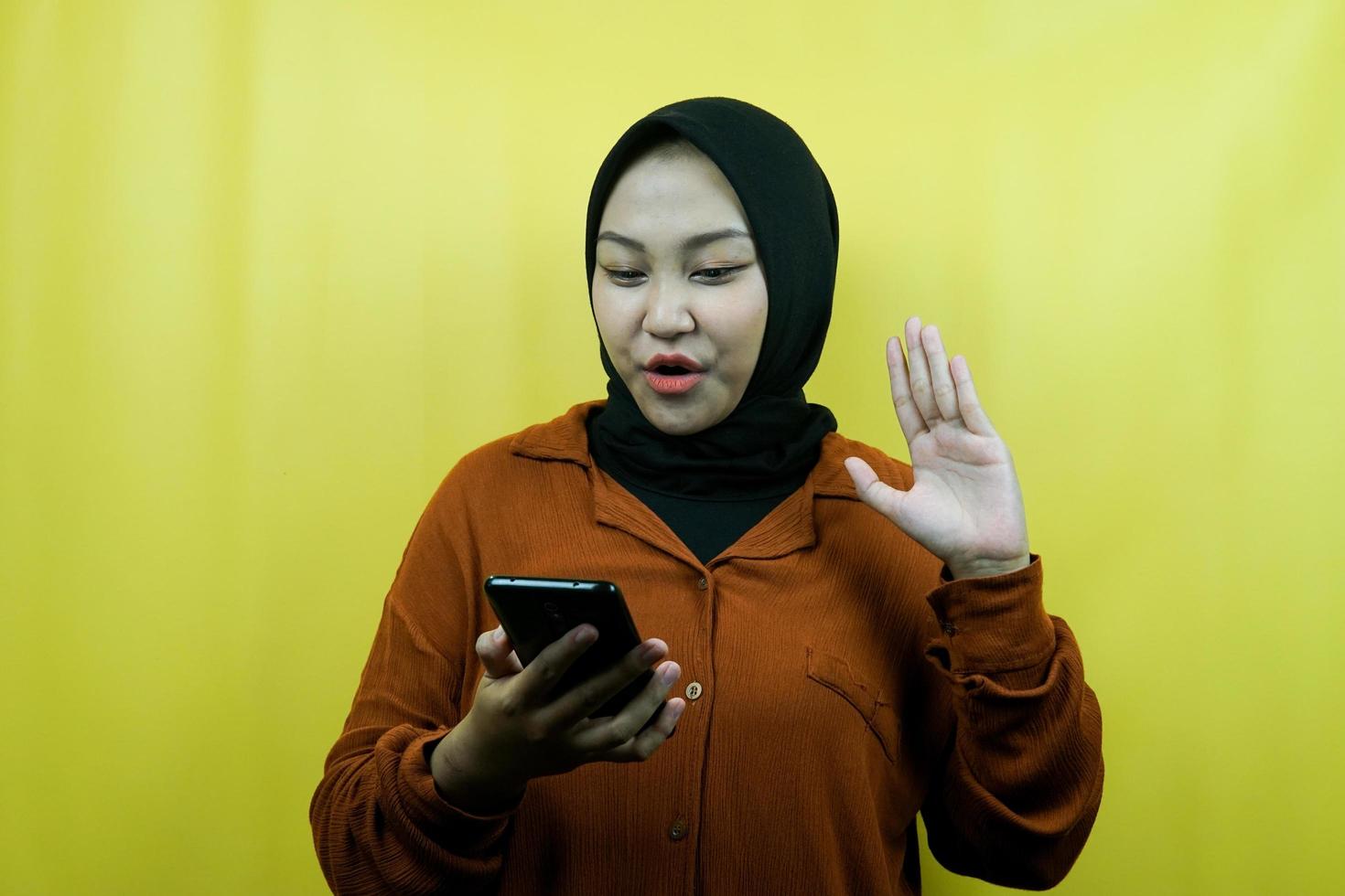 Schöne junge asiatische muslimische Frau schockiert, überrascht, mit den Händen, die Smartphone halten, Smartphone betrachten, Promo betrachten, isoliert, Werbekonzept foto