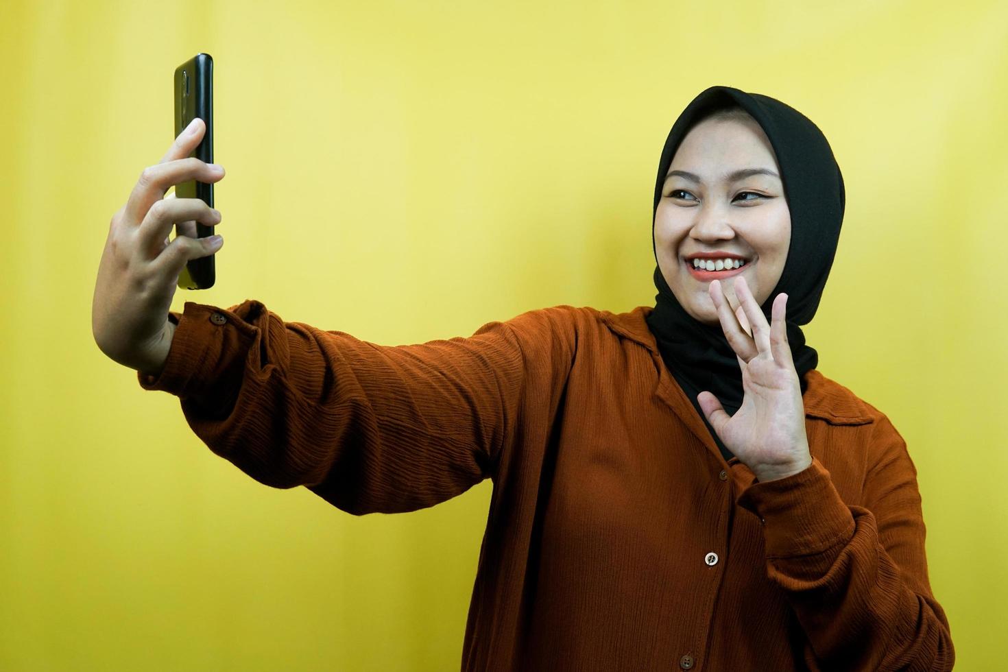 Schöne junge asiatische muslimische Frau mit Händen, die Smartphone halten, jemanden anrufen, Videoanrufe tätigen, Selfie machen, selbstbewusst lächeln, enthusiastisch und fröhlich isoliert, Werbekonzept foto