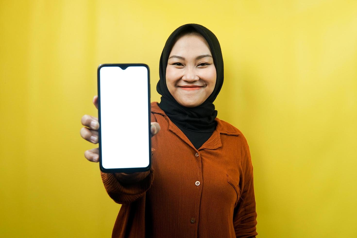 schöne junge asiatische muslimische frau, die ein smartphone mit weißem oder leerem bildschirm hält, app fördert, etwas fördert, isoliert, werbekonzept foto