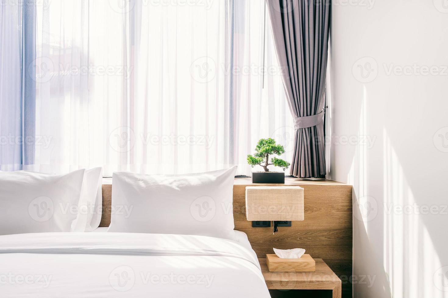 Nahaufnahme des weißen Kissens auf der Bettdekoration mit Lichtlampe und grünem Baum in Blumentöpfen im Hotelschlafzimmerinnenraum. foto