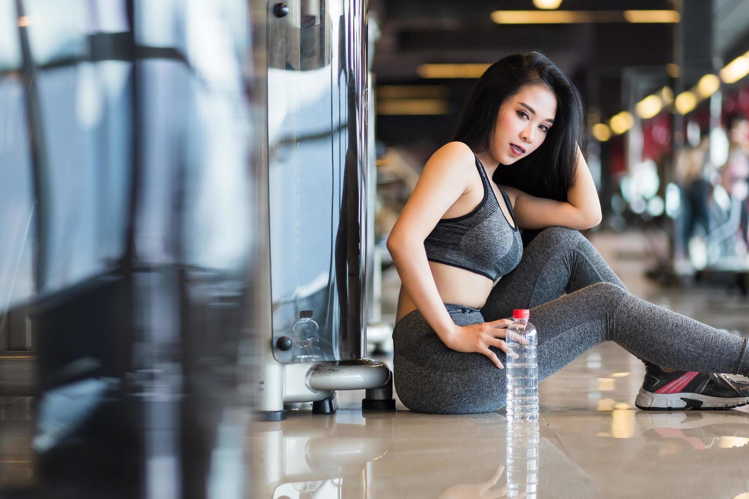 asiatische Fitnessfrauen, die im Sportstudioinnenraum und im Fitness-Gesundheitsclub mit einer Flasche Wasser sitzen. foto