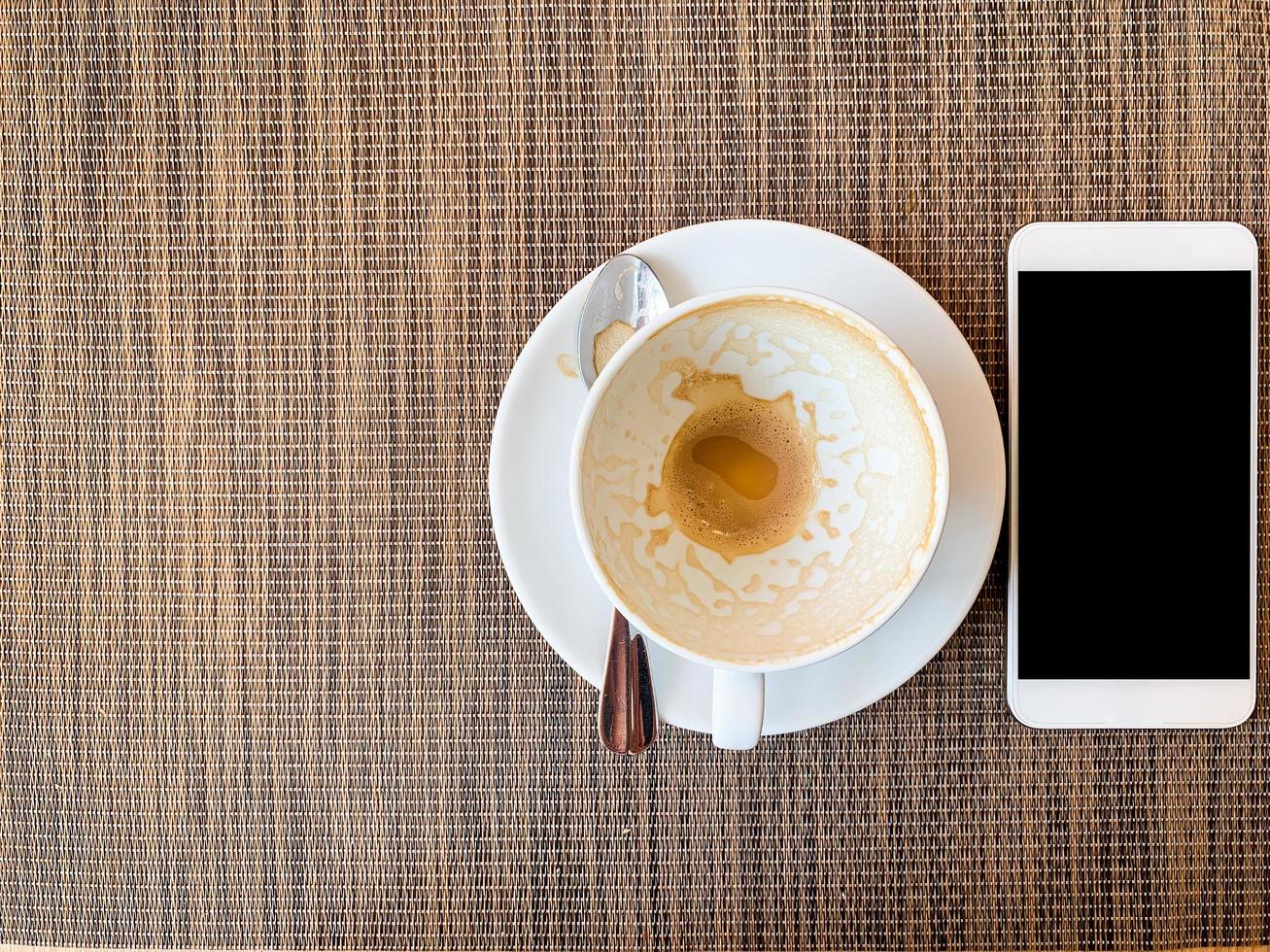 Smartphone und leere Kaffeetasse auf dem Schreibtisch aus Holz in der Draufsicht. foto