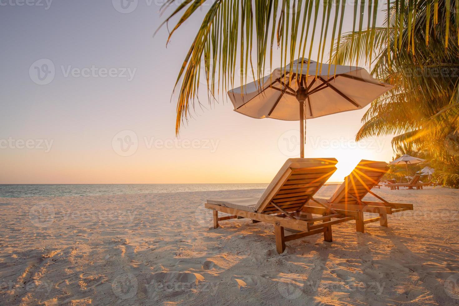 wunderschöne tropische Sonnenuntergangslandschaft, zwei Sonnenliegen, Liegestühle, Sonnenschirm unter Palmen. weißer Sand, Meerblick mit Horizont, bunter Dämmerungshimmel, Ruhe und Entspannung. inspirierendes Strandresorthotel foto