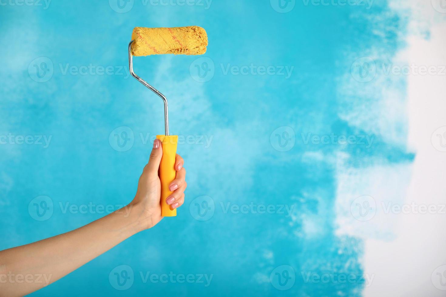 Nahaufnahme der weiblichen Hand, die gelbe Farbrolle über blauem Hintergrund hält - Reparatur-, Bau- und Bauwerkzeugkonzept. praktisches und vielseitiges Werkzeug zum Streichen von Wänden. foto