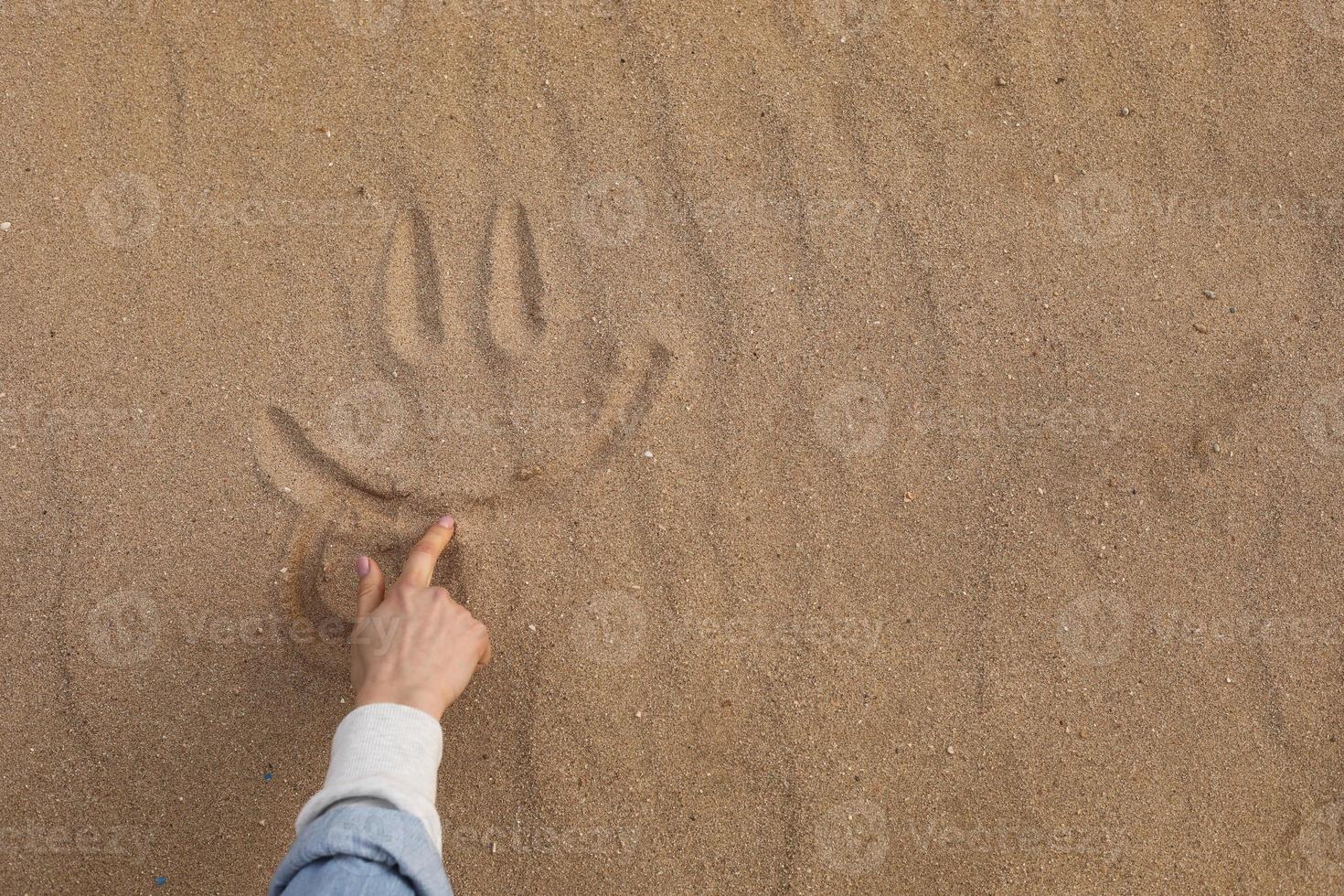 Hand, die ein schönes süßes Lächeln im Wüstensand zeichnet - Hintergrund foto
