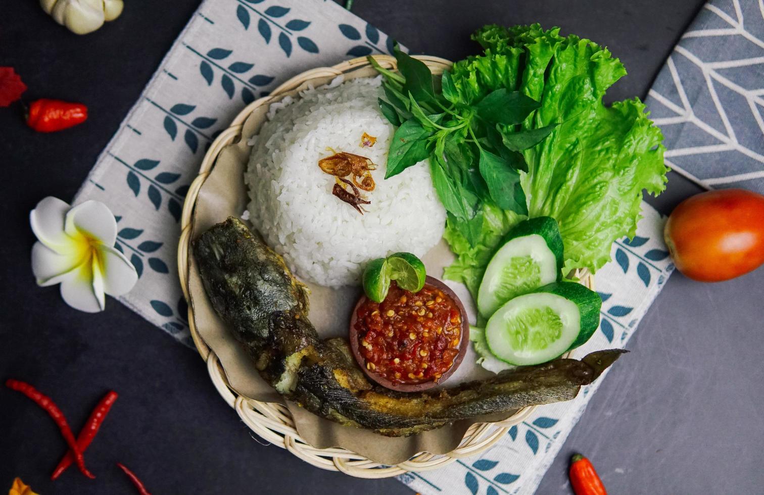 eine Packung Reis, gebratener Fisch und etwas frisches Gemüse auf schwarzem Hintergrund foto