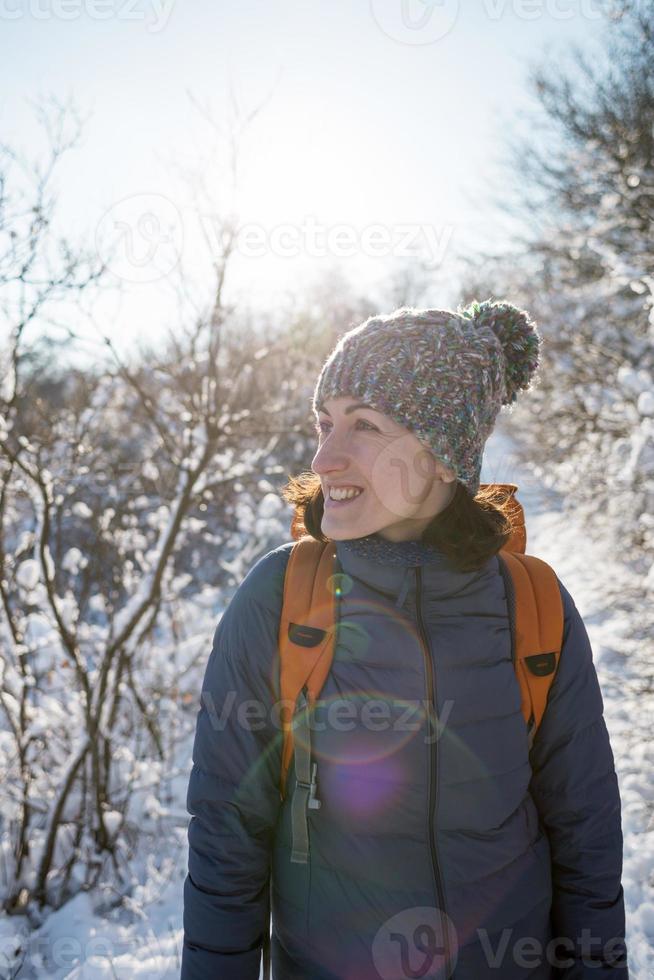 lächelnde Frau mit Rucksack auf dem Hintergrund eines verschneiten Waldes foto