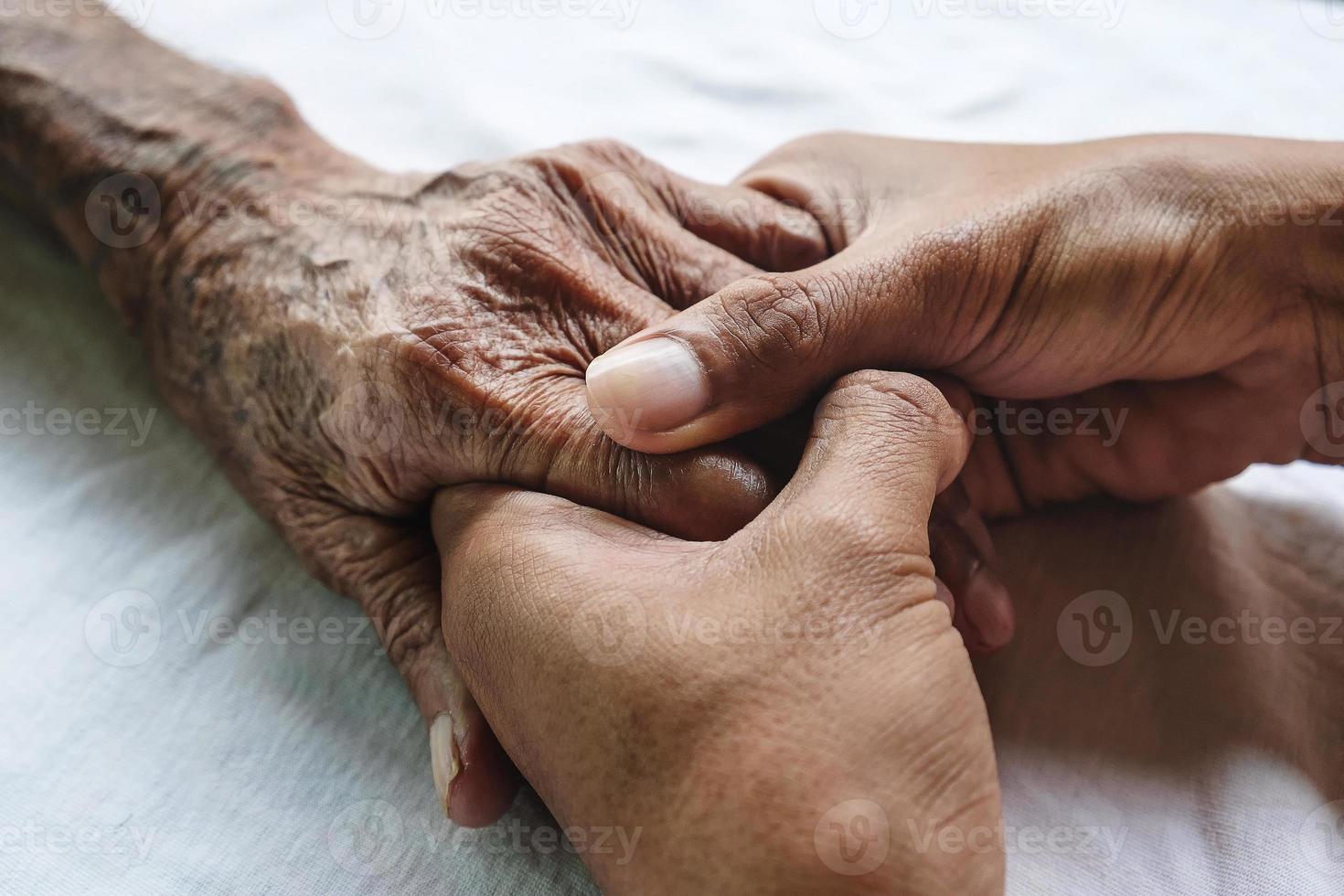 Hände des alten Mannes und eine Männerhand auf dem weißen Bett foto