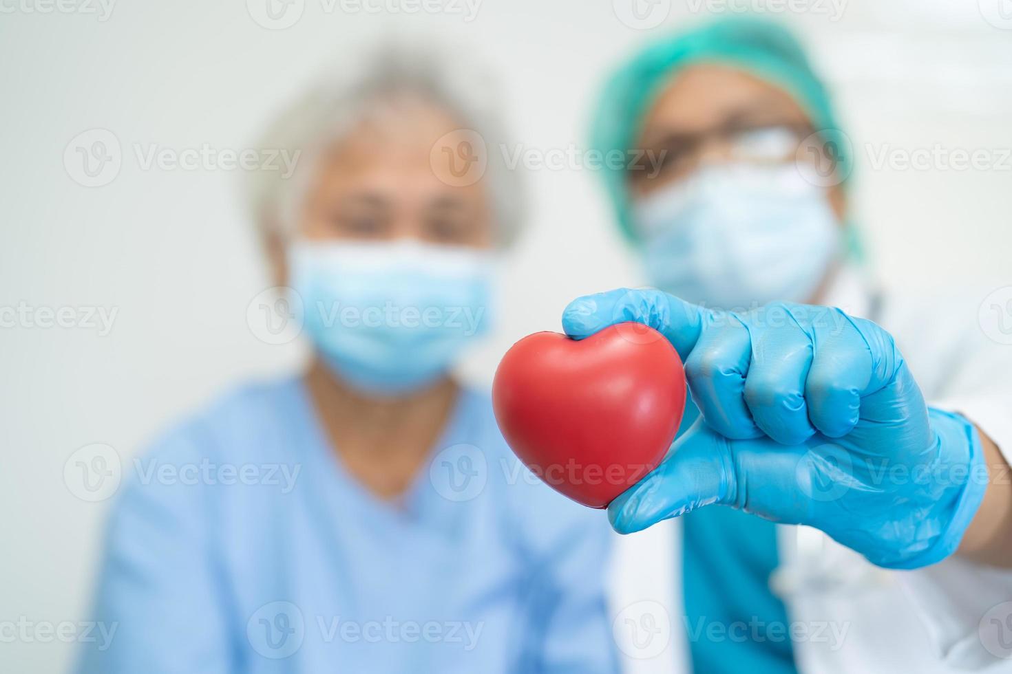 arzt, der ppe mit maske trägt, hält rotes herz zum schutz des coronavirus mit asiatischen senioren oder älteren alten patienten foto