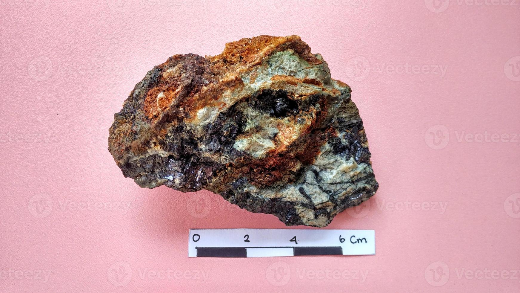 eruptiver Andesit, der in einer hydrothermalen Alterationszone alteriert ist, mit Erzgangquarz, Chlorit und glänzenden schwarzen Pyritmineralien auf einem rosa Hintergrund. Indonesien, geologische Erkundung. foto