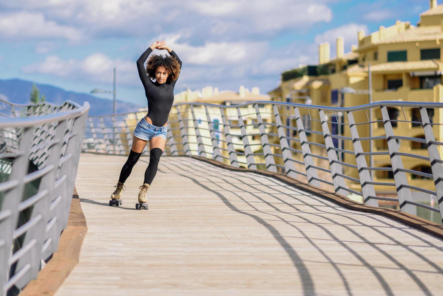 Afro-Frisur Frau auf Rollschuhen, die draußen auf der städtischen Brücke reitet foto