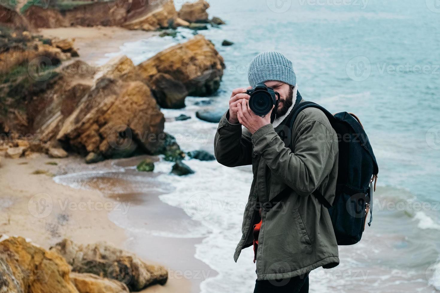 Mann Fotograf Reisender mit Rucksack Fotografieren auf Meer und Felsen Hintergrund foto