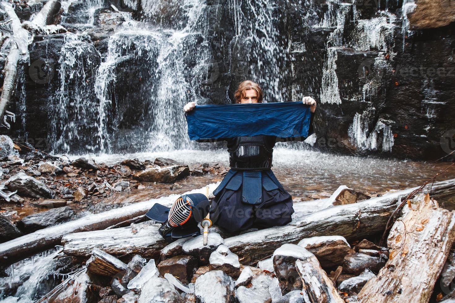 Mann, der Kendo mit Bambusschwert auf Wasserfallhintergrund übt foto