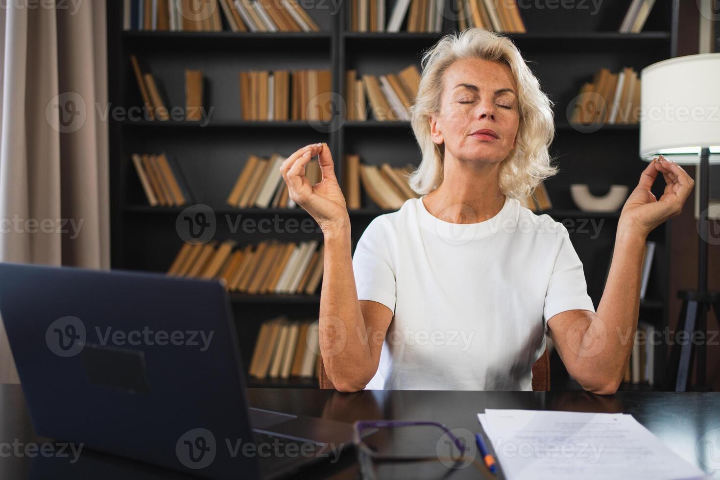 Yoga Achtsamkeit Meditation Nein Stress behalten Ruhe. Mitte alt Frau üben Yoga beim Büro. Frau nehmen brechen von Arbeit meditieren entspannend. reifen Dame tun Atmung trainieren online Yoga beim Arbeit foto