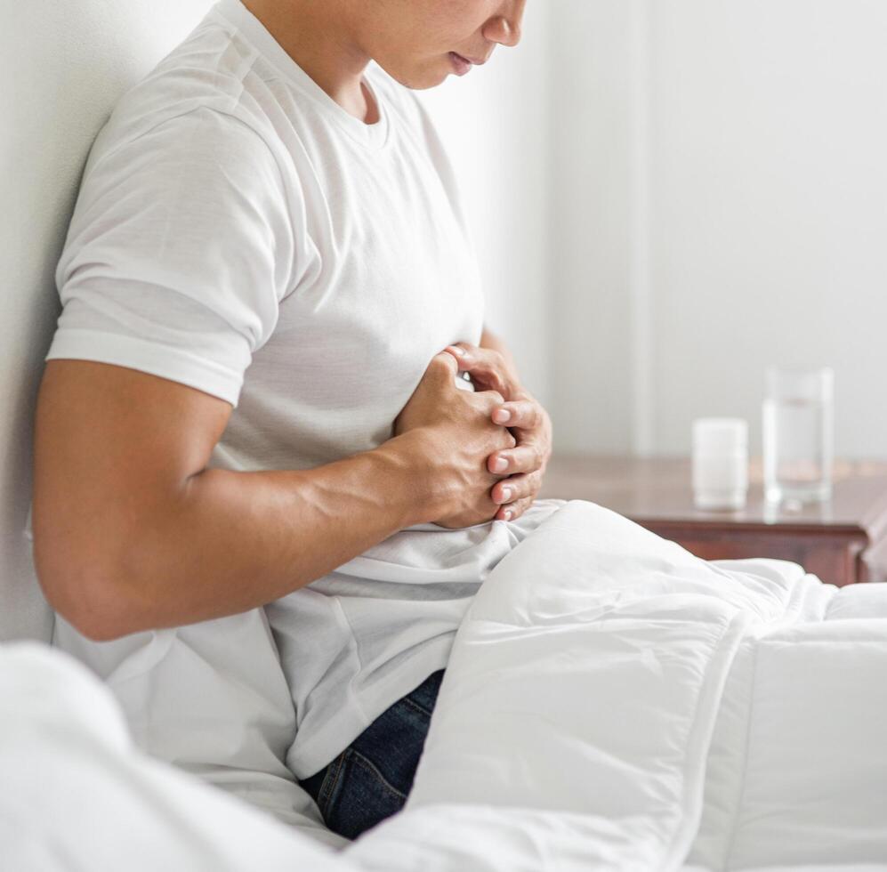 ein Mann sitzt mit Bauchschmerzen im Bett und drückt sich mit den Händen den Bauch. foto