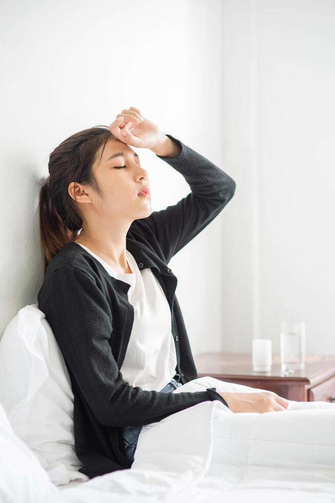 eine unbequeme Frau sitzt auf dem Bett und hat Medikamente auf dem Tisch. foto