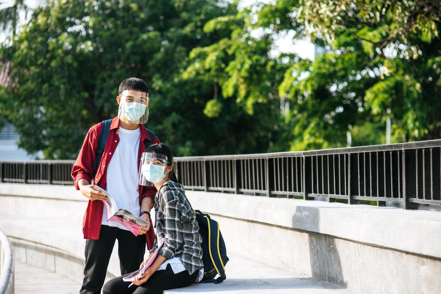 männliche und weibliche Studenten mit Masken sitzen und lesen Bücher auf der Treppe foto