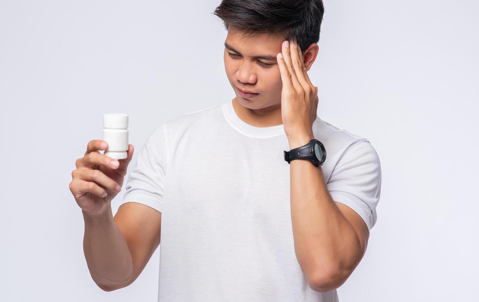 ein Mann mit Schmerzen in der Hand hält eine Medizinflasche und die andere Hand aber auf dem Kopf foto
