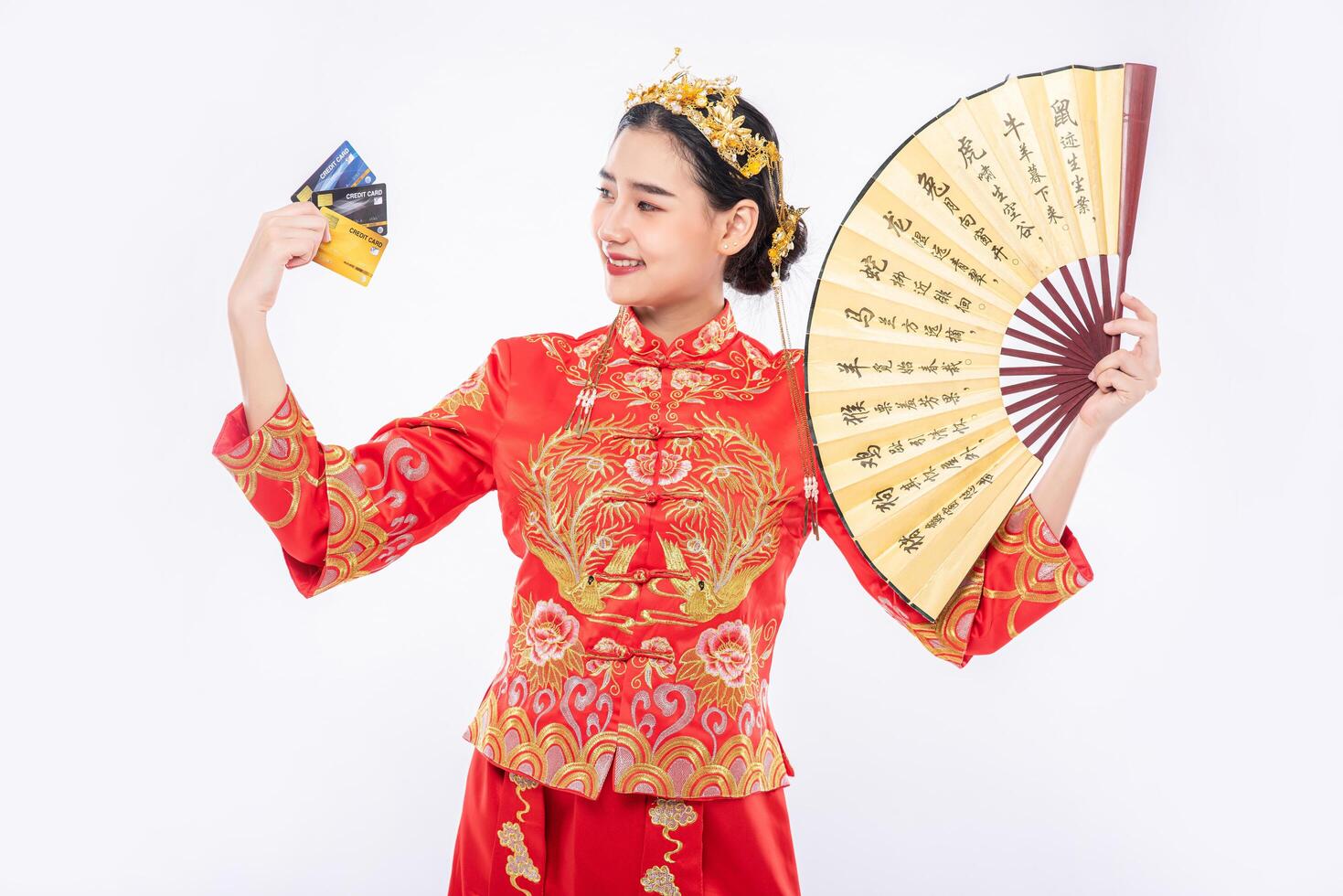 Frau trägt Cheongsam-Anzug Halten Sie den chinesischen Handfan, zeigen Sie, dass die Kreditkarte zum Einkaufen im chinesischen Neujahr verwendet werden kann foto